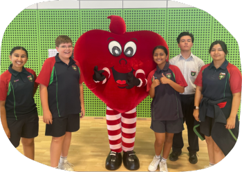 The Heart Foundation mascot, Happy Heart, standing with a group of primary school students in their gymnasium The Heart Foundation mascot, Happy Heart, standing with a group of primary school students in their gymnasium
